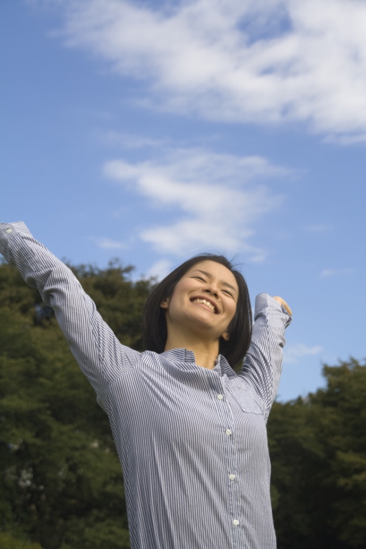 女性が青空の下、伸びをしている写真
